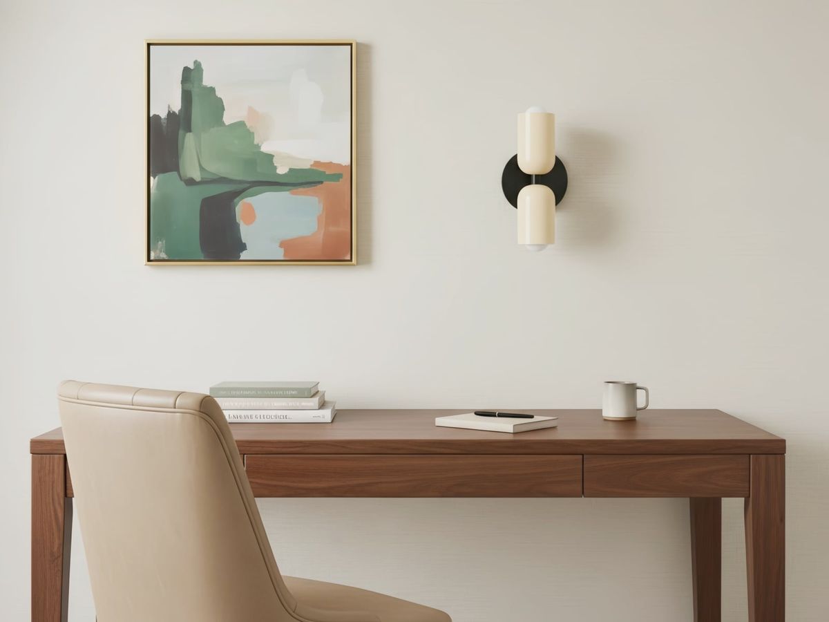 Krämvit och svart vägglampa helt synlig över ett skrivbord