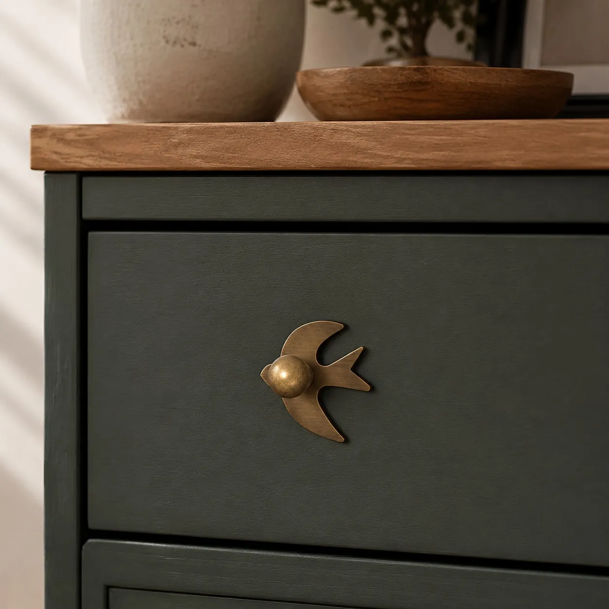 Antique brass swallow cabinet knob on a dark green drawer